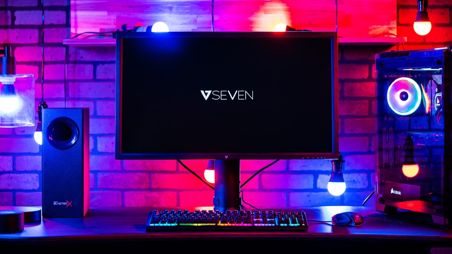 Seven Ultra HD 4K Monitor facing forward on a desk next to a gaming rig, all set in RGB-lit lighting