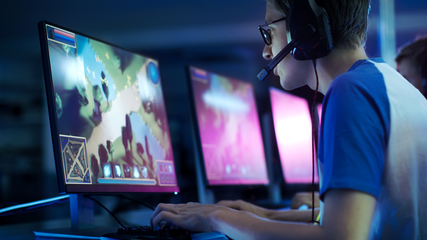 Professional eSport Gamer Playing in Competitive MMORPG/ Strategy Video Game during a Tournament. The gamer is wearing a headset in an arena filled with cool neon lights.