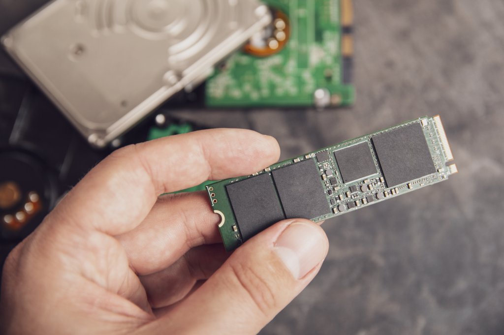 Man's hand holding modern M.2 drive with an old HDD disks in the background